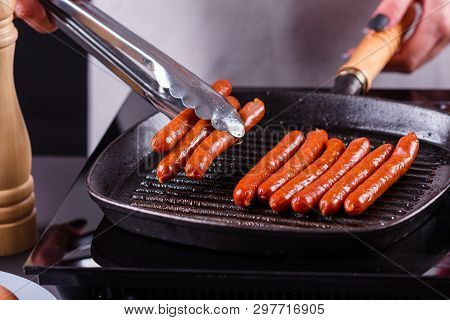 Young Woman In A Gray Apron Fries Sausages