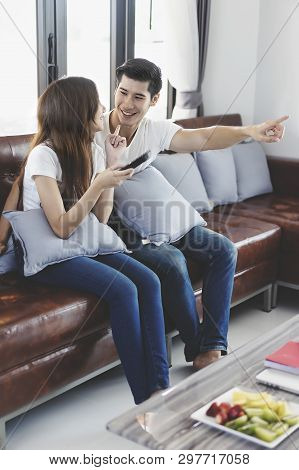 Happy Asian Young Couple Loving On The Couch Watching A Movie Together, Woman Holding Remote And Her