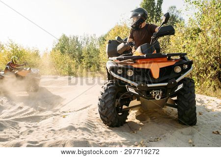 Two atv riders in helmets ride in a circle on sand