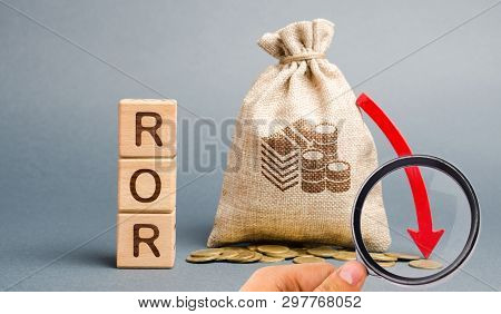 Wooden Blocks With The Word Ror, Money Bag And Down Arrow. Financial Ratio Illustrating The Level Of