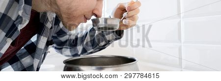 Young Man Tasting The Soup In The Ladle While Cooking At The Kithcen