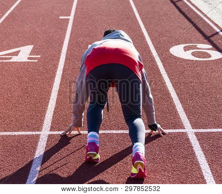 A High School Teenage Girl Is In The Set Position Ready To Sprint Down The Straightway Of A Track Du