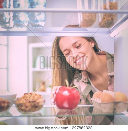 Portrait Of Female Standing Near Open Fridge Full Of Healthy Food, Vegetables And Fruits. Portrait O