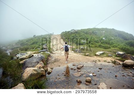 Traveler Walking In The Mountains On Foggy Summer Day. A Man Crossed The Mountain Stream. Hiking Tra