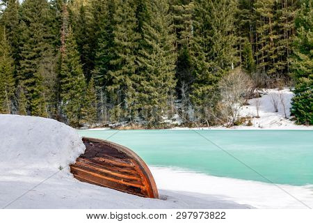 Old Wooden Destroyed Flooded Fishing Boat Lie In Snow On Shore Of Ice-covered Frozen River In Winter