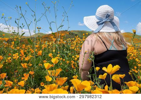 Blonde Woman Wearing A Straw Bonnet Hat Looks Out To The Field Of Poppy Wildflowers During The Super