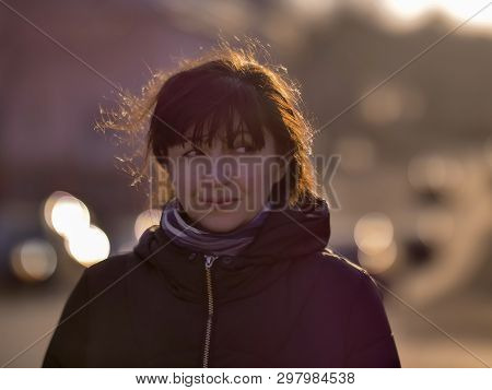 Portrait Of A Young Brunette Woman On A City Street In The Rays Of The Sun, Looking Sideways