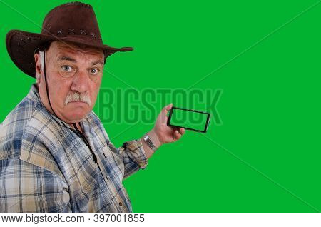 Complete Bewilderment On The Face Of The Old Farmer. In His Right Hand Is A Smartphone With A Green 
