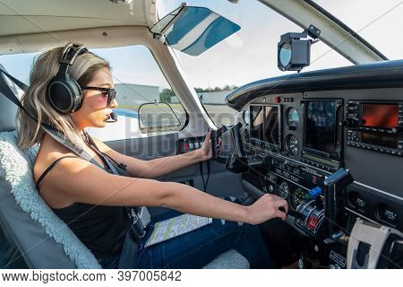 A gorgeous young blonde model poses outdoors with a single engine aircraft at a local airport