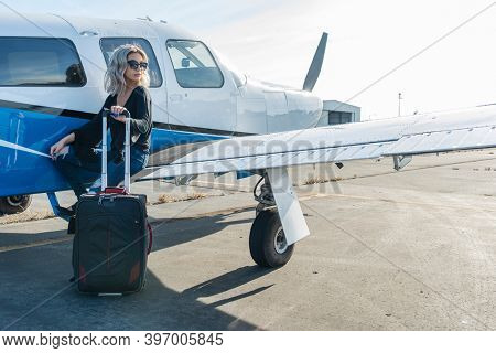 A gorgeous young blonde model poses outdoors with a single engine aircraft at a local airport