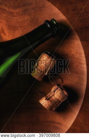 Flat lay still life of a champagne bottle and corks onb a round wooden platter. 