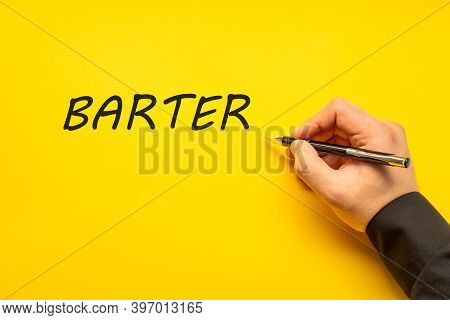 Male Hand Writes In Black Pen The Word Barter On A Yellow Background With Copy Space. Business Conce