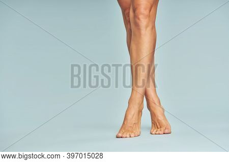Depilation Concept. Cropped Shot Of Beautiful Female Legs With Soft Silky Skin Over Blue Background