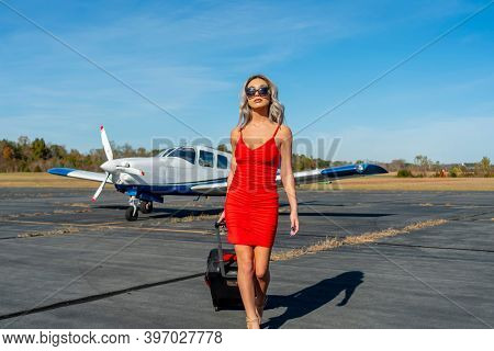 A gorgeous young blonde model poses outdoors with a single engine aircraft at a local airport