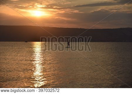 Man Sail On A Sup Board In A Large Lake During Sunrise. Stand Up Paddle Boarding - Active Recreation