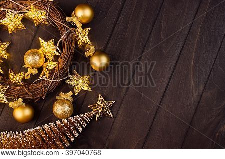 Cozy Dark Christmas Background With Golden Balls, Spruce, Wreath, Stars On Glowing Garland On Brown 