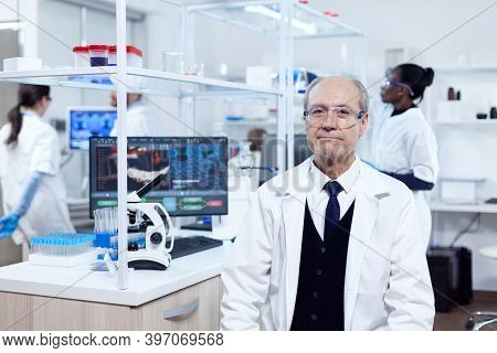 Senior Man With Virus On Computer Display Looking At Camera With Protective Glasses. Elderly Scienti