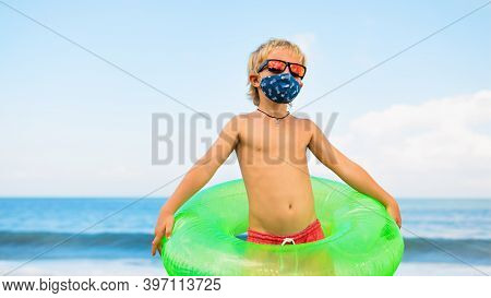 Funny Child In Sunglasses, Inflatable Ring On Tropical Sea Beach. New Rules To Wear Cloth Face Cover
