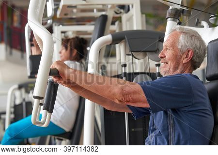 Senior Man Training At Gym, Side View. Elderly Caucasian Man Training On Machine At Fitness Club. Tr