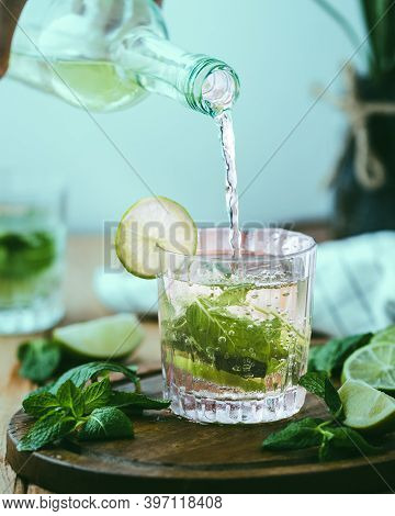 Poring Water In Glass With Mint And Lemons