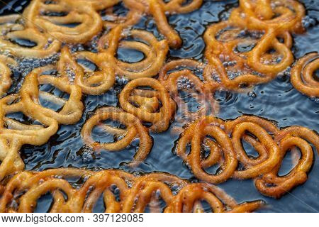 Frying Jalebi Batter In Oil. Red And Orange-colored Batter Will Be Dipped Into Sugar Syrup For A Swe