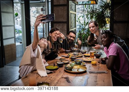 A Multicaltural Group Of Students Taking Photos Of Themselves, Making Crazy Faces. In A Cafe.