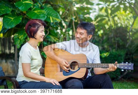 Middle Aged  Couple Playing Guitar While Relax Sitting On Bench In Backyard.
