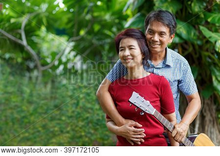 Middle Aged  Couple Playing Guitar While Relax Sitting On Bench In Backyard.