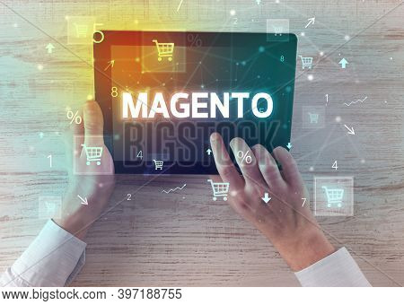 Close-up of a hand holding tablet with MAGENTO inscription, online shopping concept