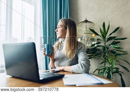 Adoult Woman 35s Working On Laptop At Home, Work From Home, Looking At Window. Stay Safe During Coro