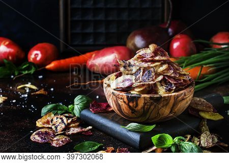 Chips From Purple And Red Potatoes In Wooden Bowl On Background Of Vegetables, Selective Focus