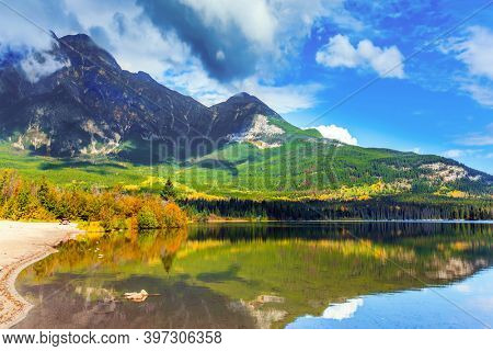 Pyramid Lake reflects Pyramid Mountain. Active eco and photo tourism concept. Rocky Mountains of Canada. Smooth water of the lake and lush cumulus clouds. 