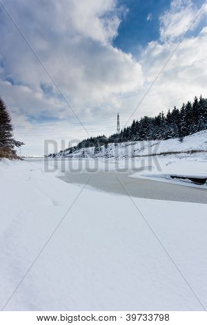 Zamrzlé jezero obklopené sníh a stromy