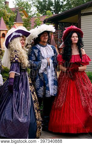 Two Young Ladies In Luxurious Vintage Dresses With A Man, Also In Vintage Clothes.puppet Museum, Jul