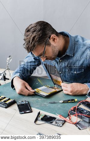 Repairman In Eyeglasses Looking At Disassembled Broken Digital Tablet Near Screwdriver And Multimete