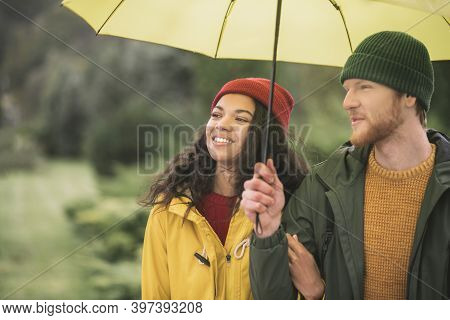 Young Couple Under Yellow Umbrela Looking Contented