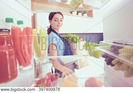 Portrait of female standing near open fridge full of healthy food, vegetables and fruits. Portrait of female