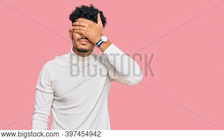 Young arab man wearing casual winter sweater covering eyes with hand, looking serious and sad. sightless, hiding and rejection concept 