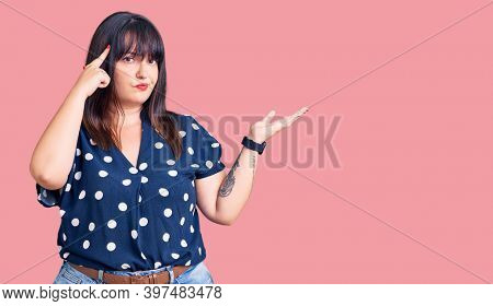 Young plus size woman wearing casual clothes confused and annoyed with open palm showing copy space and pointing finger to forehead. think about it. 