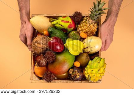 Fresh Exotic Fruits In Wooden Box Top View In Male Hands. Fruit Dragon, Papaya, Maracuya, Kiwi, Mang