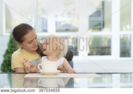 Mom With Child In Cafe Drinks Coffee. Babysitter And Toddler