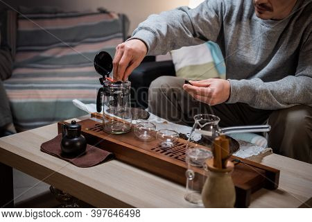A Man Learns To Conduct A Tea Ceremony At Home On His Own. Pours Black Ripe Tea With Clip Into A Tea