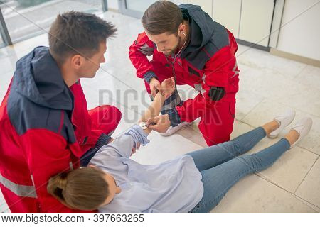 Two Medical Workers In Red Uniform Halping A Faint Woman