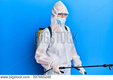 Covid specialist wearing decontamination protective suit and disinfectant spray, decontaminate and sanitize surface, standing over blue background