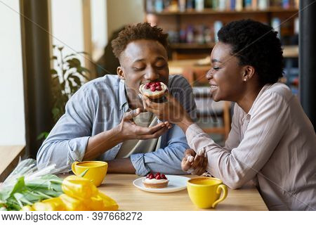 Lovely Black Woman Feeding Tasty Berry Tartlet To Her Boyfriend At Cozy City Cafe. Affectionate Afri