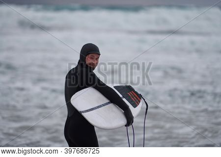 Arctic surfer going by beach after surfing