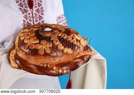 Woman With Korovai On Light Blue Background, Closeup. Ukrainian Bread And Salt Welcoming Tradition