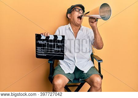 Handsome mature director man holding video film clapboard and louder angry and mad screaming frustrated and furious, shouting with anger looking up. 