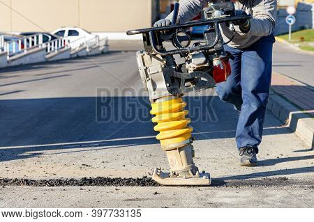 A Road Worker Operates A Vibratory Rammer To Asphalt A Small Area On A Bright Sunny Day. Copy Space,