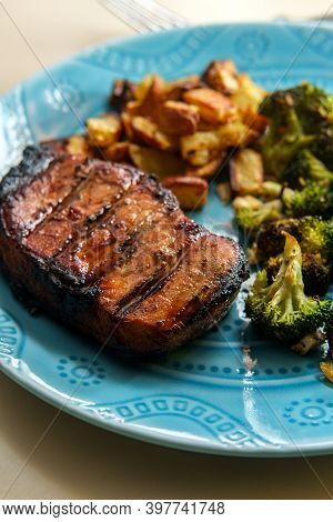 Marinated Char-grilled Pork Chops With Grill Marks Side Of Home Fries And Broiled Broccoli